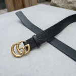 Gucci womens black leather belt with a large antique gold interlocking G buckle displayed on a stone plinth (1)
