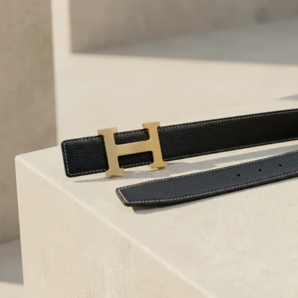 Premium womens black grained leather belt with a brushed gold H shaped buckle on a minimalist stone pedestal (6)