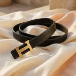 Premium womens black grained leather belt with a brushed gold H shaped buckle on a minimalist stone pedestal (9)