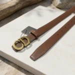 Slim chocolate brown leather womens belt with a gold CD logo buckle displayed on a stone pedestal (2)