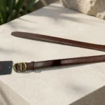 Slim chocolate brown leather womens belt with a gold CD logo buckle displayed on a stone pedestal (3)