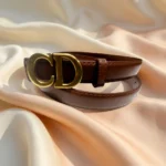 Slim chocolate brown leather womens belt with a gold CD logo buckle displayed on a stone pedestal (5)