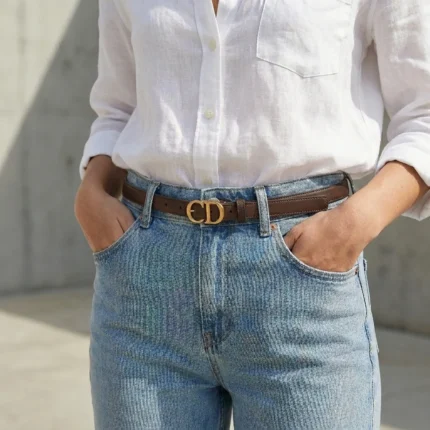Slim chocolate brown leather womens belt with a gold CD logo buckle displayed on a stone pedestal (6)