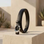 Womens slim black leather belt with silver C shaped metallic buckle on a stone pedestal (1)