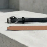 Womens slim black leather belt with silver C shaped metallic buckle on a stone pedestal (2)