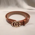 a rolled tan womens belt with a large gold interlocking buckle on a stone pedestal (1)